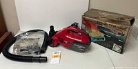 Eureka Model 55 red handheld vacuum cleaner, flexible hose, various attachments and original box.