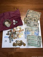 Overview of all currency items on a table including Canadian bills, coins, tokens, and pendants in a cloth bag
