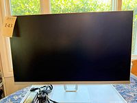Front view of the 27-inch HP Pavilion monitor with the screen off, silver stand and base, with black power adapter and cables placed in front.