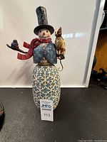 Full front view of the Jim Shore Heartwood Creek snowman figurine standing against white background, showing full body, hat, scarf, cat, and bird, with lot tag visible.