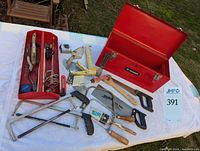 Photo showing red Husky tool box, take-out tray and assorted hand tools including hacksaws, hammer, scrapers, tape measure, utility knife and paintbrushes spread on white surface.