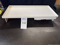 Photo of the white monitor stand showing its rectangular shape, top platform surface, and drawers underneath.
