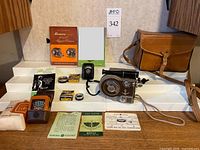 Full display of all items included in the lot: Revere Eight Model 70 camera with strap, leather carry case, three light/exposure meters, two filters, film boxes, manuals, and associated accessories on white surface.