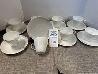 Set of 8 white porcelain cups and saucers with embossed pattern laid out on fabric surface.