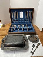 Full view of the flatware set in wooden case and plated serving dishes and utensils displayed on a table.