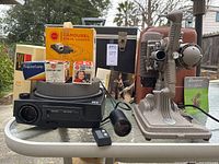 Full lot including Revere Eight projector on right side, Kodak Carousel 760H projector on left, accessories like projector lamps, Carousel slide tray, stack loader, manuals, and carrying cases.