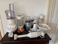 Full lot photo showing all appliances: Cuisinart food processor/blender, Magic Bullet blender with box and accessories, Braun immersion blender, and KitchenAid hand mixer.