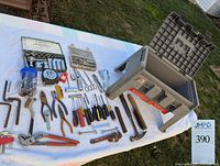 Wide view of gray step stool tool box open on a cloth outdoors along with assorted hand tools laid out for display.