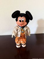 Front view of vintage Mickey Mouse doll dressed in cream jacket and orange hakama standing on dark surface.