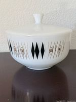 Side view of vintage white milk glass casserole bowl with lid showing black diamond and gold atomic harlequin pattern
