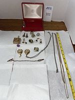 Photo showing full spread of jewelry laid out on white paper towel with red jewelry box open in back, tape measure displayed for size reference.