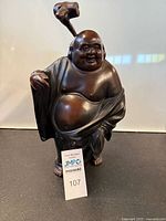 Front view of bronzed cast iron Laughing Buddha statue showing detailed facial features, robe folds, and the removable stick hatch element.