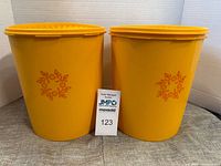 Pair of vintage yellow Tupperware canisters with orange wreath design on side, placed next to each other with lot tag in front.
