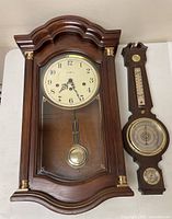 Front view of Howard Miller wall clock and Springfield weather station side by side showing clock face, pendulum and weather instruments