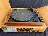 Full view of Weathers turntable on original box, showing walnut wood tonearm and frame, black metal platter and controls.