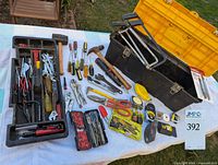 Assorted hand tools and toolbox tray laid out on white cloth outdoors