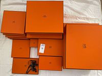 14 Hermes orange boxes arranged on a white cloth. Boxes vary in size.