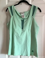 Full front view of mint green Adidas tank top hanging on black hanger.