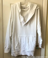 Front view of white Aerie sweatshirt hoodie hanging on door, showing the hood, V-neck style, and dual front pockets at waist level.