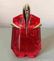 Front view of red glass perfume bottle with gold spray nozzle top, uniquely shaped bottle resembling Alien Fusion design.