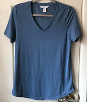 Front view of Athleta V-neck T-shirt, slate blue color, hanging on hanger showing full front.