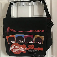 Front view of black messenger bag featuring The Beatles portraits and Hard Days Night text and guitar graphic.