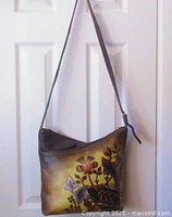Full view of handpainted leather crossbody bag showing floral design on front, brown leather strap hung on door.