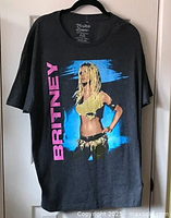Full view of the grey Britney Spears t-shirt hanging, showing front graphic with Britney image and pink vertical text.