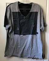 Full view of light grey V-neck t-shirt with black faux leather rectangular design on front hanging on plastic hanger.