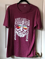 Full front view of purple-red short sleeve t-shirt hanging on hanger showing full graphic and text