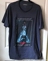 Navy blue t-shirt hanging showing full front graphic of Jaws movie poster and quotes.