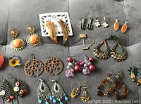 Photo of assorted costume jewelry including earrings, ring, and pins arranged on a grey surface.