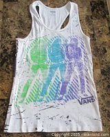 Front view of white tank top showing blue, green, purple graffiti style print of three skateboarders and VANS logo at bottom right.