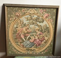 Front view of vintage framed tapestry with rural Victorian scene showing two ladies and one man playing instruments, sitting on grass surrounded by floral border.