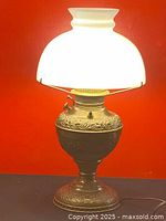 Lighting lamp illuminated showing brass embossed base and milk glass shade
