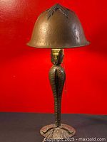 Full view of the antique Roycroft hammered brass lamp with helmet-shaped shade against a red background.
