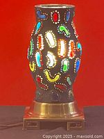 Front view of black art glass lamp shade with colorful raised abstract patterns, lit from inside, set against a red background.