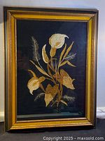 Full framed embroidery artwork showing calla lilies stitched on black silk with wooden frame and glass cover.