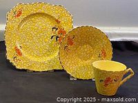 Front view of trio set and cake plate showing chintz yellow pebbled pattern with orange and black floral details.