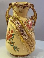 Full view of the antique ceramic vase showing embossed ribbon detail, floral patterns, and dual handles