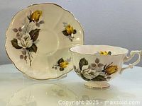 Photo showing Royal Albert teacup and saucer with yellow and white floral rose design, scalloped edges, and gold trim.