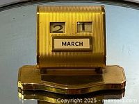 Front view of the brass perpetual calendar showing date and month windows with March and day 21 displayed.