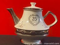 Front view showing the teapot body with 25th anniversary emblem and silver accents on lid, handle, and base.