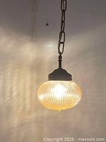 Mid-century modern style pendant lamp hanging from chain with illuminated ribbed and bubble texture globe.