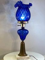 Full view of the Murano cobalt blue glass lamp with brass body and marble base on a white surface against white background.