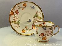 Tea cup and saucer side view showing hand painted floral and butterfly decoration with gold trim