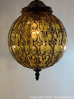 Front view of the vintage amber glass hanging lamp showing round amber globe shade with dark decorative pattern illuminated from inside.