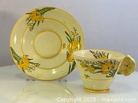 Tea cup and saucer displayed side by side, showing floral hand-painted design and flower-shaped handle.
