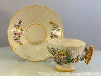 Photo showing teacup with butterfly handle and matching saucer in background, highlighting shape and floral decorations.