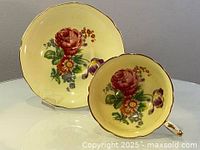 Side and angled view of the vintage Paragon teacup and saucer on a display stand showing the floral pattern and gold trim.